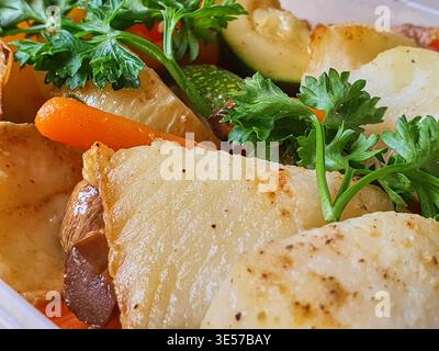 Macro close-up photograph of roasted mixed vegetables including sliced potatoes, carrots, zucchini, and mushrooms, topped with fresh green parsley Stock Photo