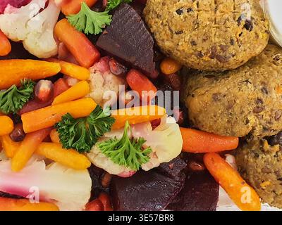 A close-up, overhead view of a colorful vegetarian meal featuring roasted baby carrots, cauliflower florets, and cubed beets arranged on a plate. The Stock Photo