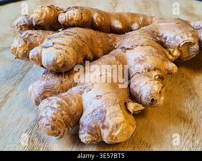 Close-up photograph of fresh raw ginger rhizomes resting on a light wooden surface. The ginger roots display their characteristic irregular, gnarled Stock Photo