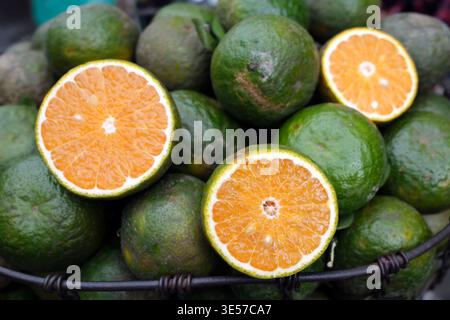 Basket of green oranges sliced in half at a street market.  Vietnam. Stock Photo