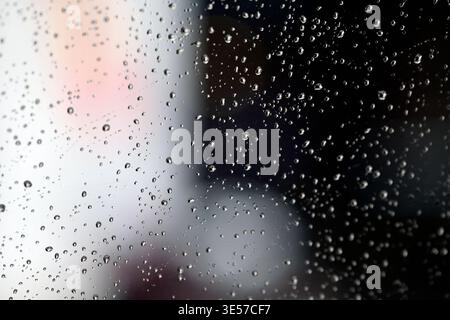 Rain drops on a window create patterns and reflect lights in the background during a rainy day.   Vietnam. Stock Photo