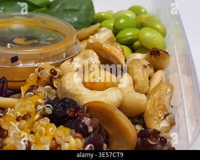 Close-up macro shot of a healthy meal prep container featuring roasted cashew nuts, bright green edamame beans, tri-color quinoa with visible Stock Photo