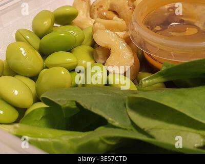 Close-up photograph of fresh healthy food ingredients in a clear plastic container. The composition features bright green shelled edamame beans with Stock Photo