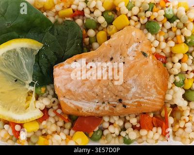 Top-down close-up view of a healthy prepared meal featuring a cooked salmon fillet seasoned with herbs and black pepper, placed on a bed of pearl Stock Photo