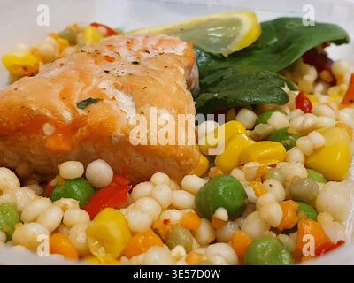 Close-up photograph of a prepared meal featuring a seasoned salmon fillet resting on a bed of Israeli couscous mixed with colorful vegetables. The Stock Photo
