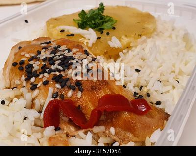A close-up photograph of a prepared meal served in a clear plastic takeout container. The dish features a piece of golden-brown glazed chicken thigh Stock Photo