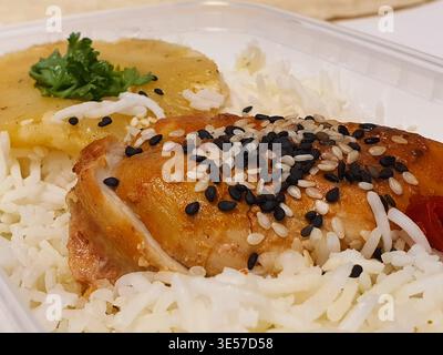 Close-up view of a prepared meal served in a clear plastic takeout container. The dish features a golden-brown roasted chicken thigh topped with Stock Photo