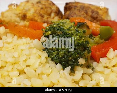 Close-up macro photograph of a healthy meal plate featuring riced cauliflower or grain in the foreground, topped with a dollop of green pesto or herb Stock Photo