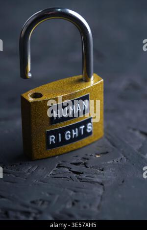 Open yellow padlock with the words Human Rights on dark textured background, representing freedom and liberation Stock Photo