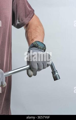 Close up worker gloved hands holding heavy metal socket wrench tool, ready for professional automotive repair work Stock Photo
