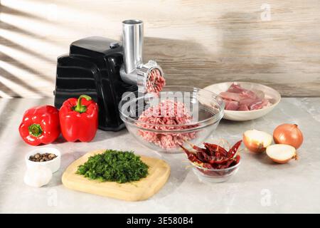 Electric meat grinder with minced meat and ingredients on grey table in kitchen, closeup Stock Photo