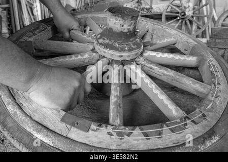 Detail shot showing hands working on a vintage, hand-painted wooden wagon wheel in a restoration workshop. The wheel features colorful patterns. Stock Photo