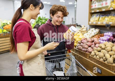 A friendly shop assistant helps a customer choose produce in a vibrant fruit store. They engage in conversation amidst colorful displays of fresh groc Stock Photo