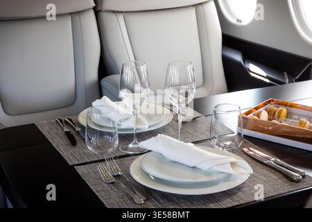 A table set for in-flight dining inside a modern executive business jet, highlighting a luxurious private aviation cabin interior. Stock Photo