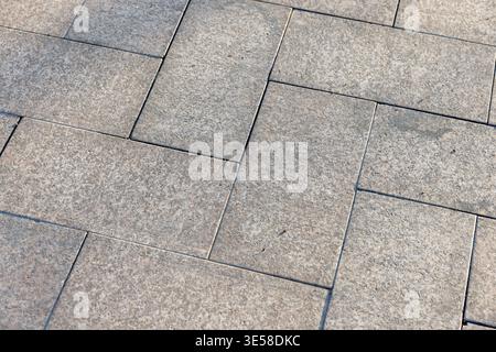 A close-up of textured stone paving tiles forming a geometric sidewalk pattern, highlighting neutral tones, grout lines and a weathered surface ideal Stock Photo