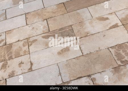 A close-up of aged beige stone tiles laid in a rectangular pattern showing weathered marks, grout lines and surface texture. Ideal for architecture, f Stock Photo