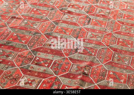 Close-up of a vintage handwoven oriental rug showing red geometric motifs and worn texture, ideal for interior design, textile, cultural, and pattern Stock Photo