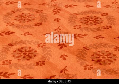 Close-up of an orange floral patterned carpet showing plush texture and repeating ornamental motif, ideal for interior design, backgrounds, textiles a Stock Photo