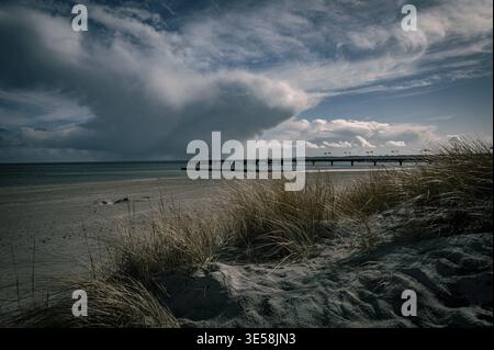 Dramatic cloud formations over a beach with a long pier in the background, the view across the sandy beach to the Baltic Sea, Suedstrand in 23775 Groï¿½ Stock Photo