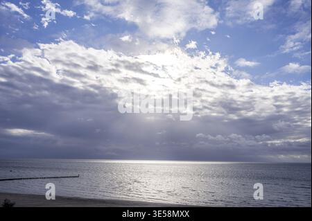 Cloudy sky over a calm sea with a beach in the foreground and rays of sunlight, the view across the sandy beach to the Baltic Sea, Suedstrand in 23775 Stock Photo