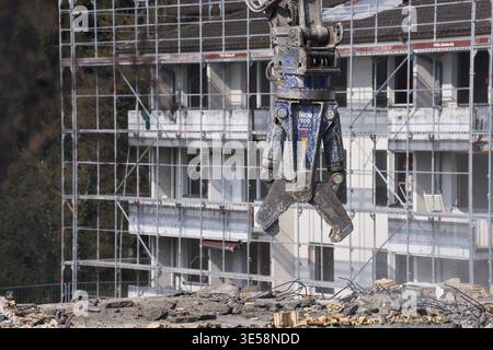 Construction site, demolition of an old building from the 1960s, excavator with hydraulic pliers, broken bricks lying around on concrete pavement, dis Stock Photo