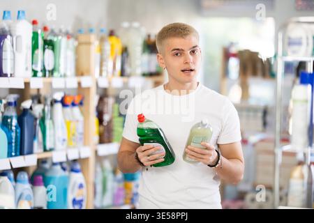 Focused young man choosing dishwashing liquid on supermarket shelf Stock Photo