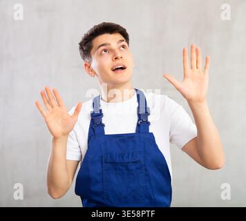 Young experienced worker in blue jumpsuit is actively gesticulating, looking up to right Stock Photo