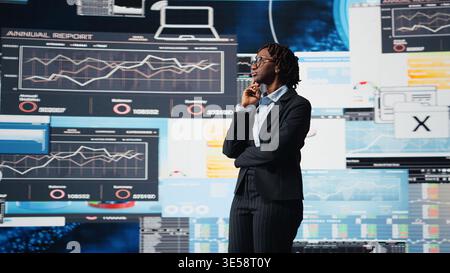Business manager looking at graphs on digital screens, thinking how to increase company profits. African american woman reading KPI metrics projected on digital screen during decision making, camera A Stock Photo