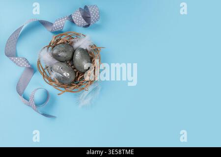 Easter eggs in nest with ribbon on blue background copy space Stock Photo