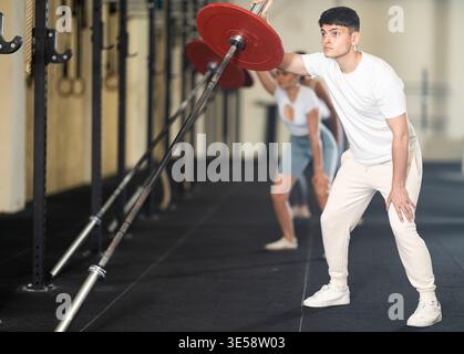Athletic young guy pumping up her arm biceps using one side of barbell Stock Photo
