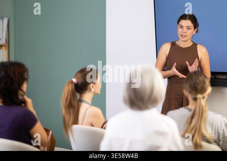 Young woman speaks to audience of listeners, carry out lecture. Stock Photo