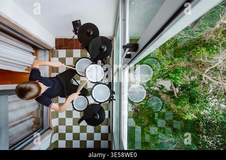 Boy playing electronic drums on balcony at home, child practicing music Stock Photo