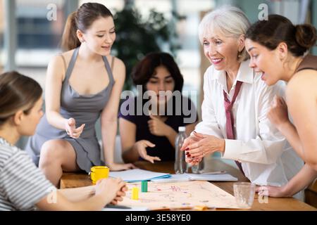 Happy office female workers different ages spending free time in office and playing logical board game, mental activity in playful way Stock Photo