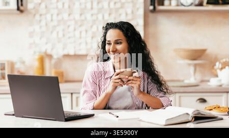 Woman Enjoys Drink While Using a Laptop at Home in the Morning Stock Photo