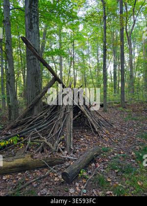 A crude lean-to of branches and sticks stacked in a heap stands near a trail in the woods in an Ohio park, seen at dusk. Stock Photo