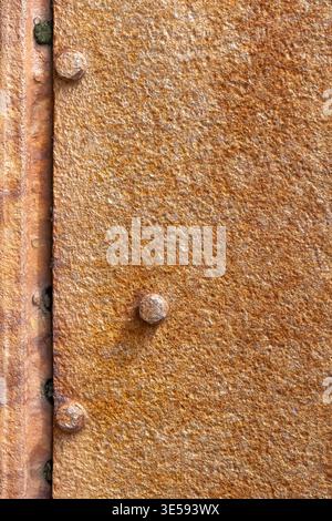 A close view of a rusty metal surface showing texture and bolts. The orange and brown colors highlight age and weathering. Stock Photo