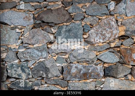 A wall made of various stones shows the rough texture and colors of the different materials used in construction. Stock Photo