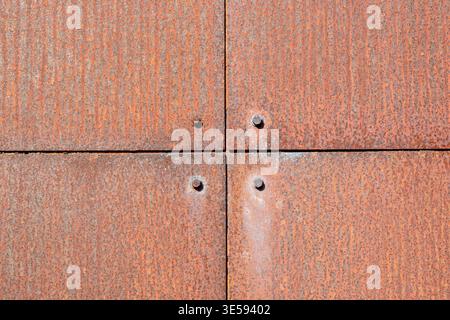 Rusty metal panels are attached to each other, forming a square layout with visible screws and texture on the surface. Stock Photo