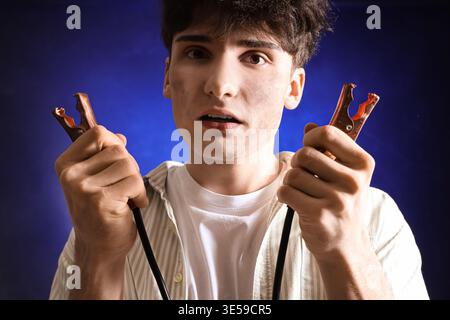Electrocuted young man with burnt face and jumper cables on dark background, closeup Stock Photo