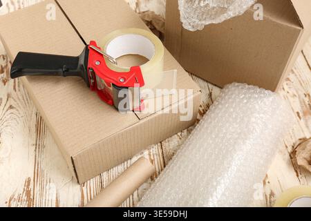 Packing tape dispenser, cardboard boxes and roll of bubble wrap on wooden background Stock Photo