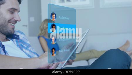 Holding adult man wearing plaid shirt using holographic contact list on couch, tablet, copy space Stock Photo
