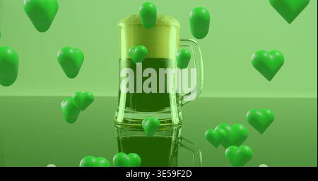 Displaying clear-glass mug holding green drink topped foam on studio table with floating hearts Stock Photo
