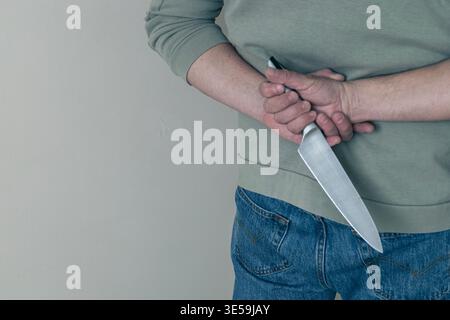 Close-up of man holding a kitchen knife behind his back, suggesting danger, threat or hidden intent. Concept of violence, crime, secrecy or potential Stock Photo