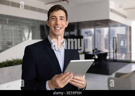 Businessman in professional attire standing in contemporary office with tablet Stock Photo