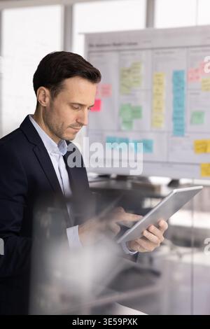 Serious mid adult businessman using tablet near sticky note roadmap Stock Photo