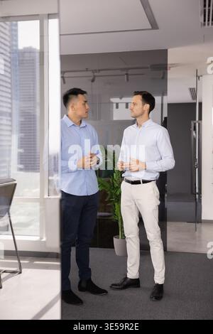 Two male business partners coworkers meeting talking in office corridor Stock Photo