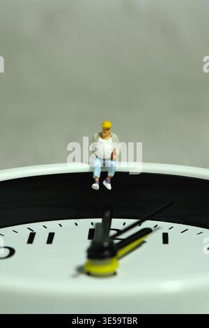Miniature people toy figure photography. Fat men worker take a break rest above clock. Image photo Stock Photo