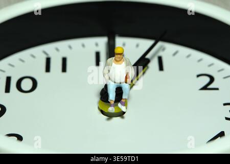 Miniature people toy figure photography. Fat men worker take a break rest above clock. Image photo Stock Photo