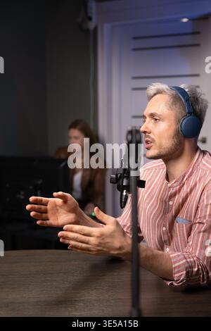 Male podcaster in headphones speaking during live recording session Stock Photo