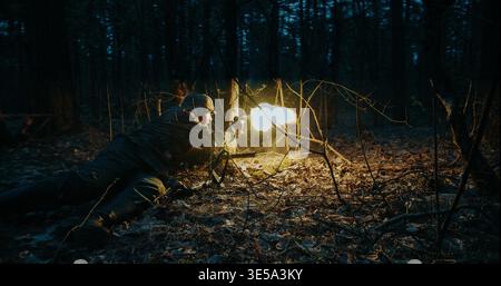Soldier firing weapon with muzzle flash in dark forest during WWII event Stock Photo